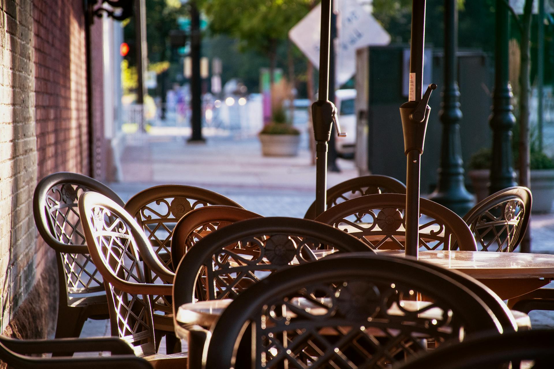 Sunlit outdoor urban patio with elegant chairs and tables on a quiet street.