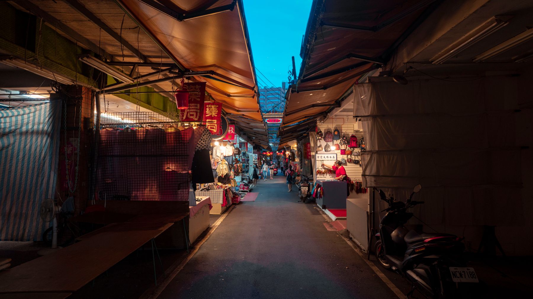 Explore a bustling night market alley with vendors and stores under colorful canopies.