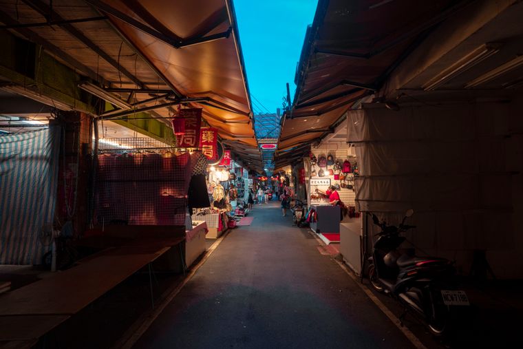 A narrow night-market alley lined with awnings and stalls at dusk — photo by Jimmy Liao on Pexels