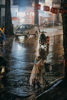 Motorbikes and cars navigate a wet urban street at night under heavy rain.