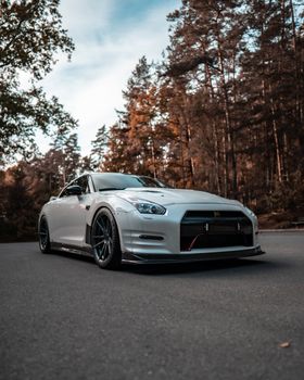 White sports car parked on an open road surrounded by autumn trees, highlighting its sleek design.