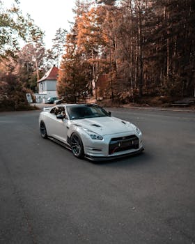 A sleek white Nissan GT-R photographed on a scenic road surrounded by lush trees in autumn colors.