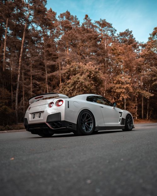 Free White sports car parked on a scenic forest road, showcasing luxury and speed. Stock Photo