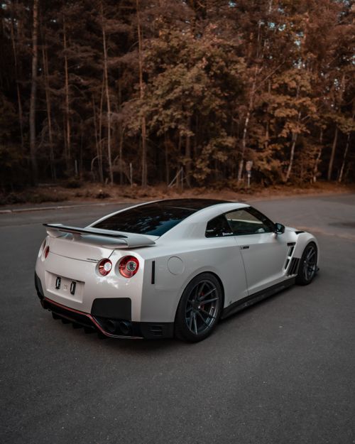 Free A sleek white Nissan GTR parked on a forest road, showcasing its sporty design. Stock Photo