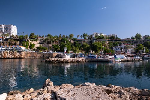 Free Beautiful harbor scene with boats, a lighthouse, and surrounding greenery on a sunny day. Stock Photo
