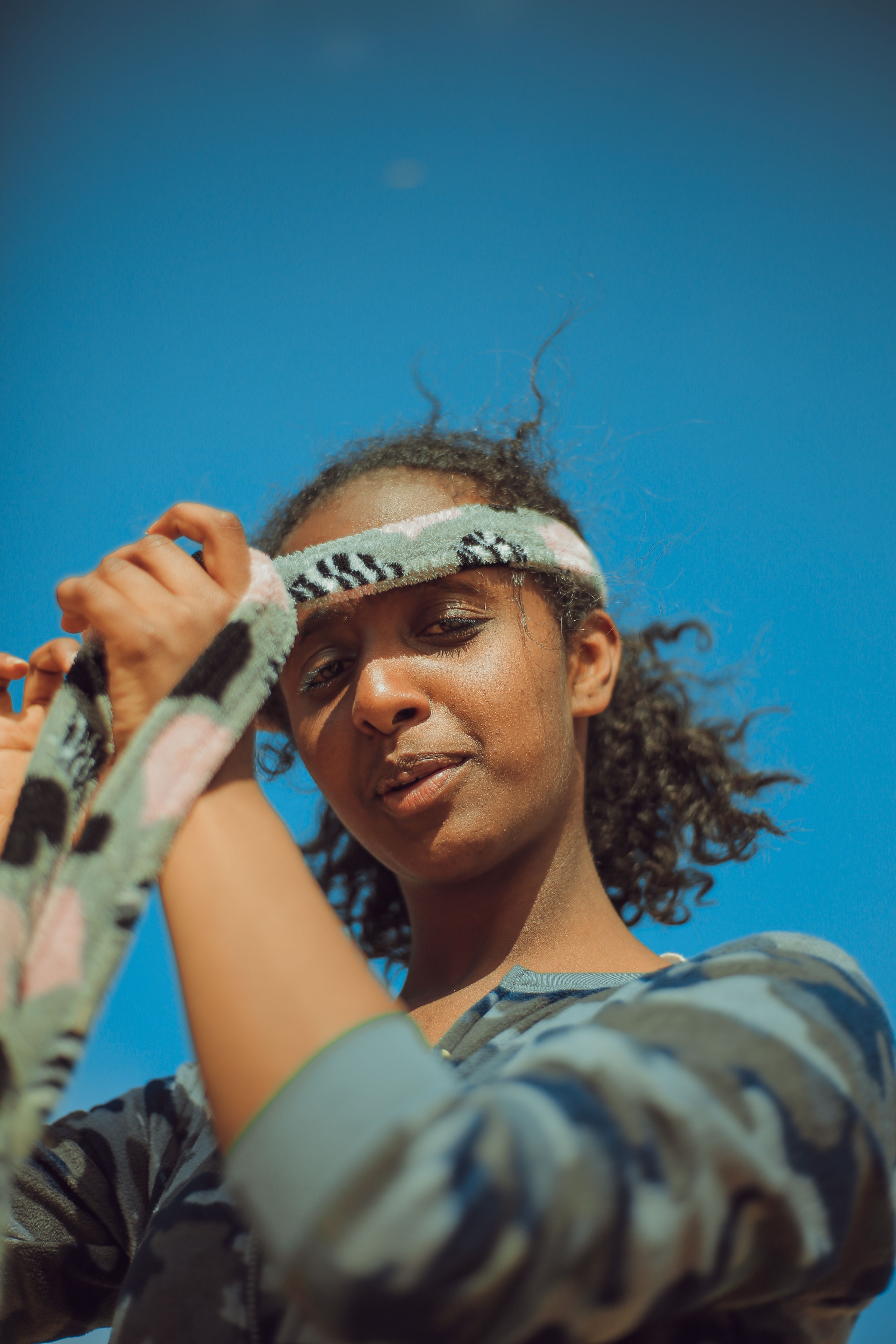African woman adjusting her headband with a clear blue sky background in Addis Ababa.