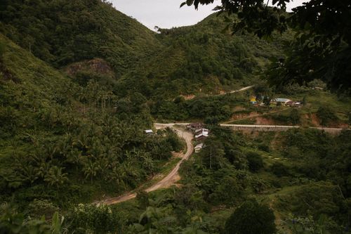 Free Explore a picturesque rural landscape with verdant hills and a winding unpaved road. Stock Photo