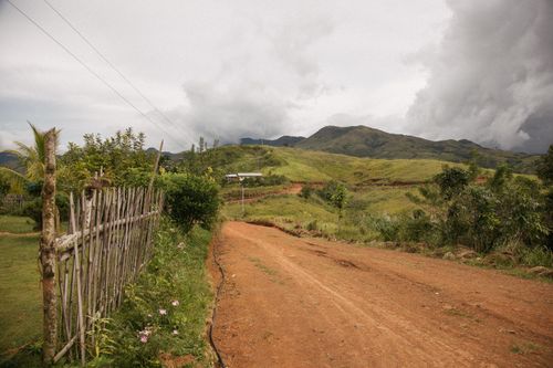 Free Picturesque rural landscape featuring a winding dirt road, vibrant greenery, and looming mountains under a dramatic sky. Stock Photo