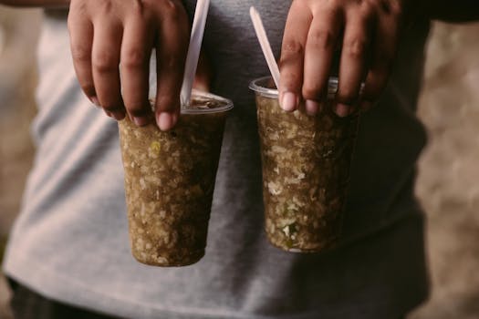 Close-up of hands holding two iced drinks in plastic cups with straws, perfect for a hot day.