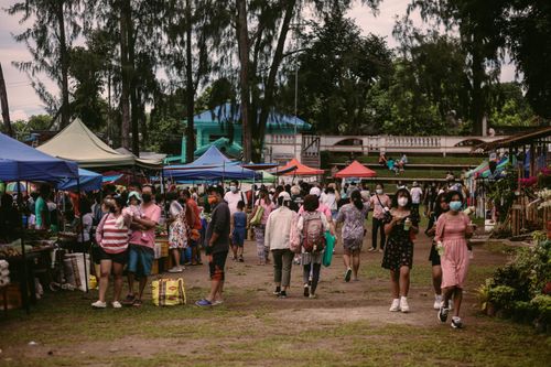 Free Bustling outdoor market scene with people wearing masks and colorful stalls. Stock Photo