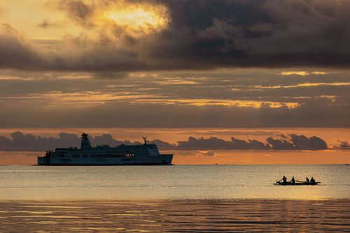 Free A scenic view of a ferry and canoe silhouetted against a stunning sunset over calm seas. Stock Photo