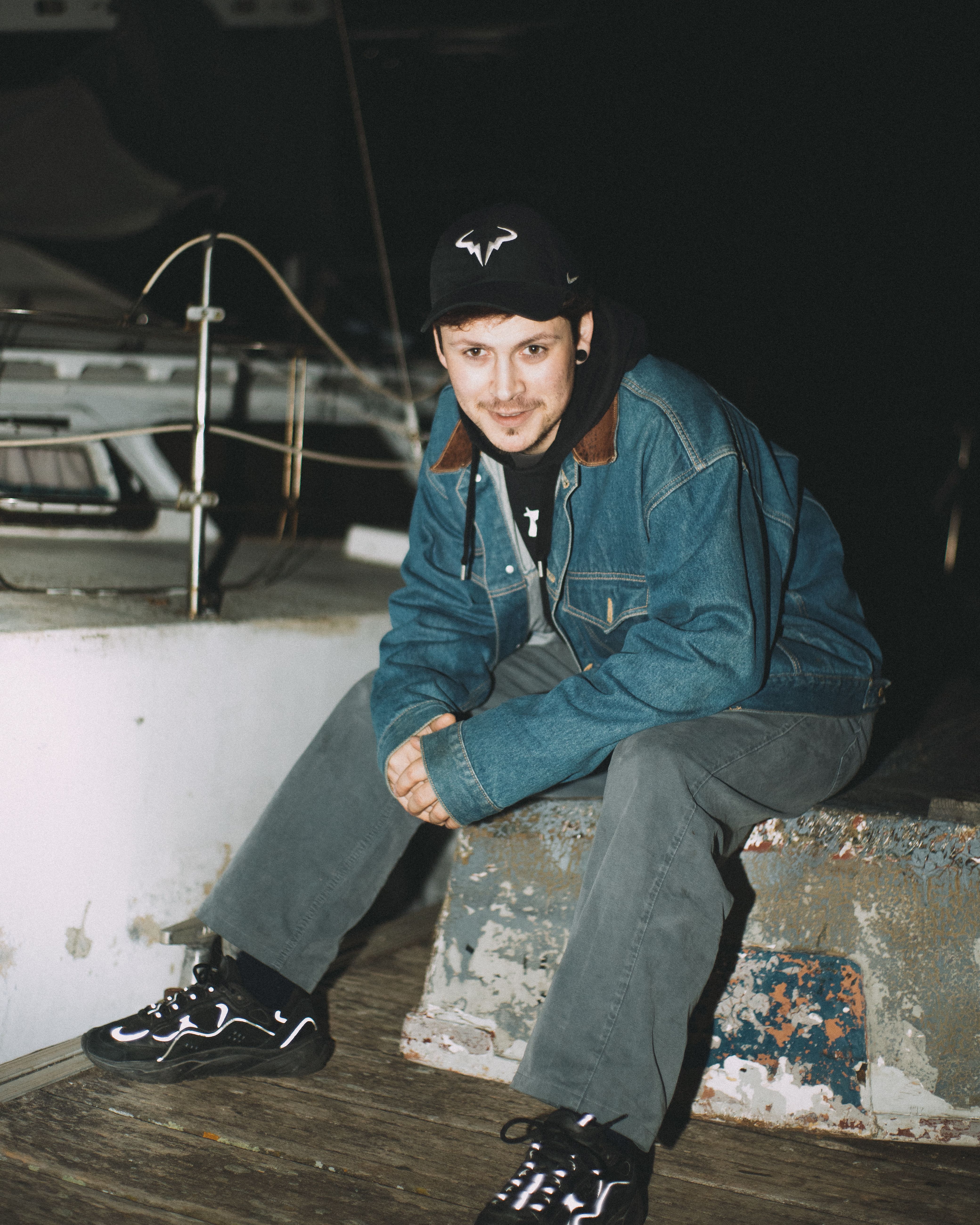 A relaxed man in a denim jacket sitting outdoors at night on a concrete bench.