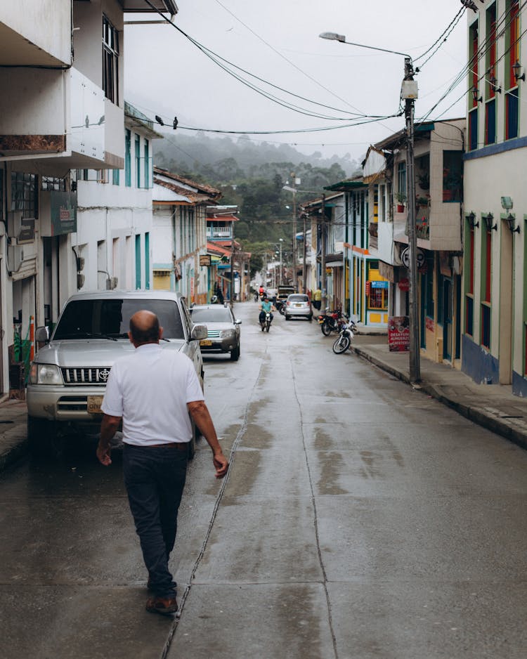 A Man Walking On The Street Near Parked Cars