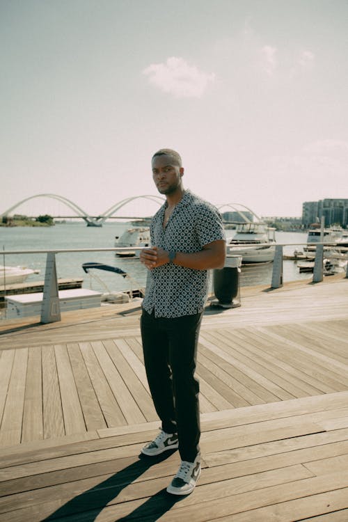 Man in Blue Polo Shirt and Black Pants Standing on Wooden Dock