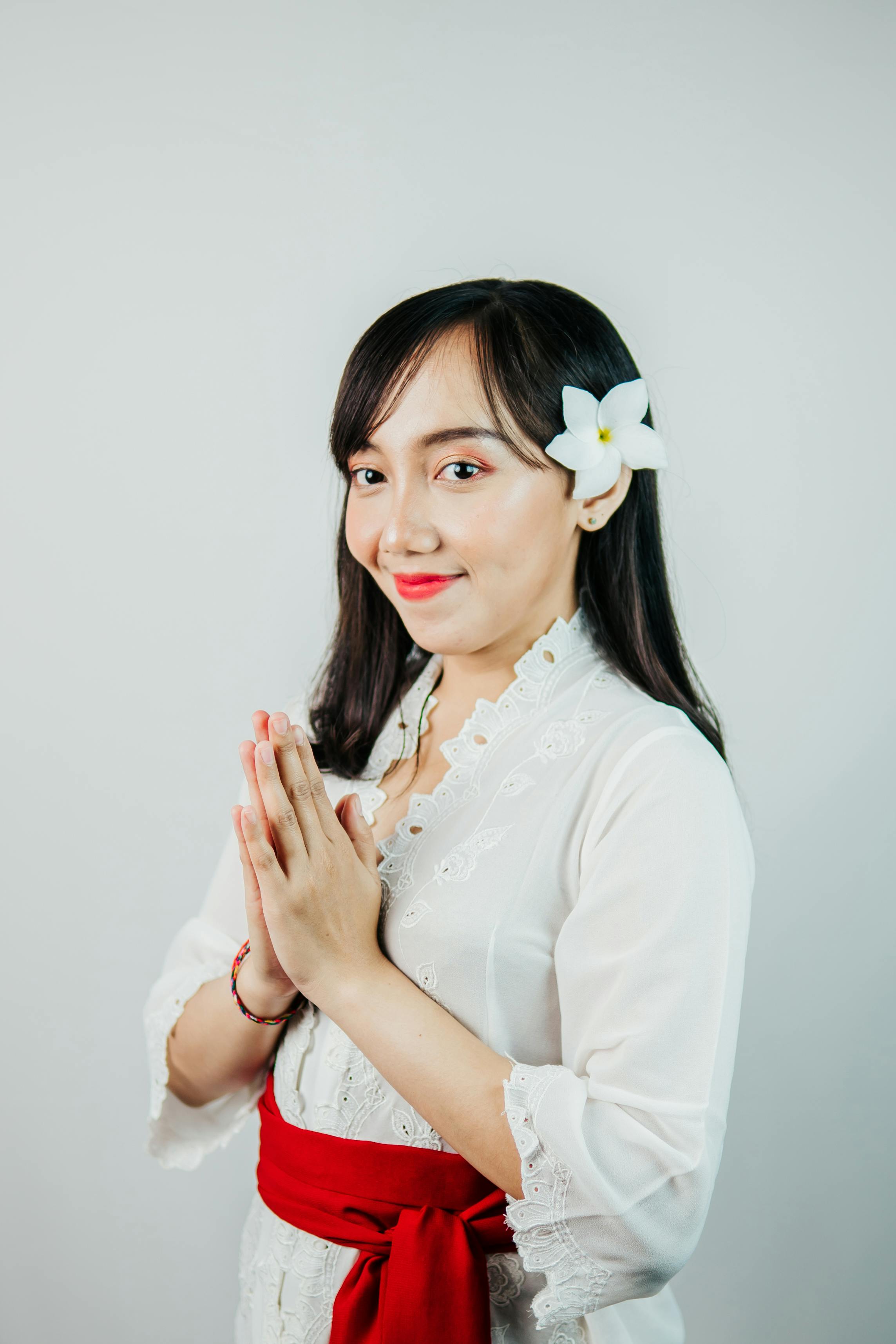 Portrait of a Balinese woman in traditional attire, featuring a frangipani flower and red sash.