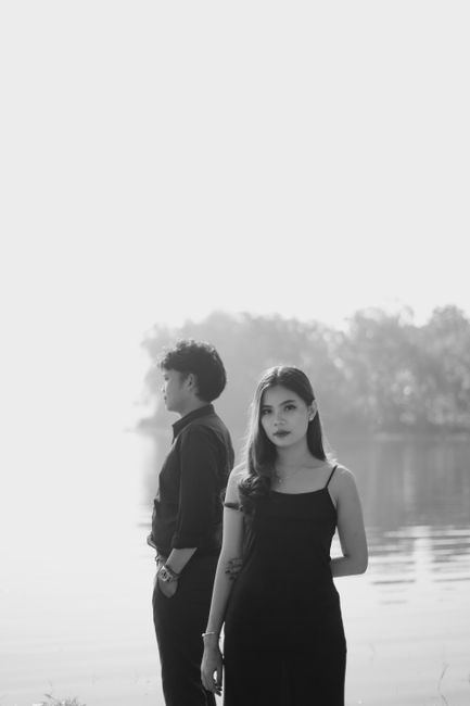 Elegant black-and-white shot of a couple standing by a serene body of water.