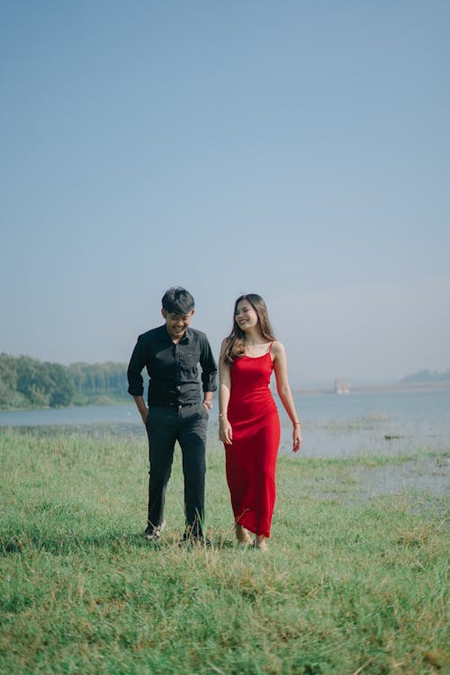 Free A Couple Walking on Grass near Body of Water Stock Photo