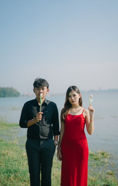 A couple in formal attire holding white flowers by the lake, creating a romantic ambiance.