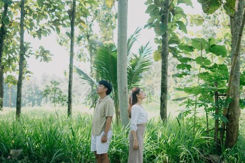 Free Asian couple standing back-to-back in a vibrant Indonesian forest. Stock Photo