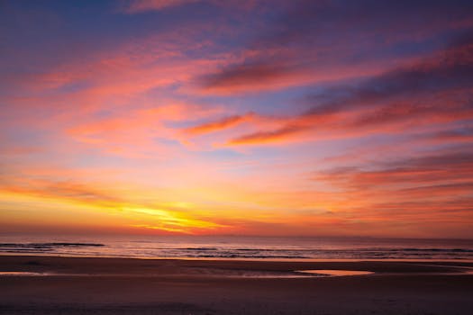Experience the serene beauty of a sunrise on Daytona Beach, capturing warm hues over the Atlantic Ocean.
