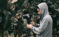 Man in Hooded Jacket Holding Camera With Stablizer