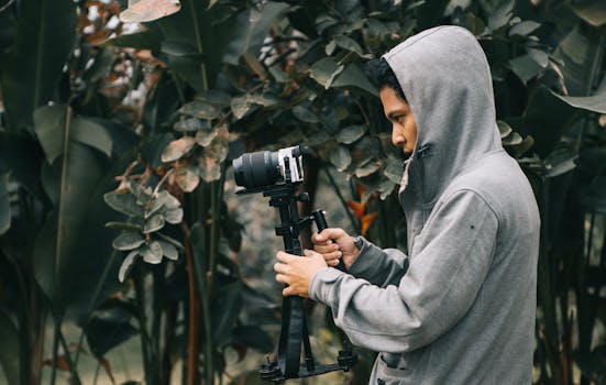 Photographer using a camera stabilizer outdoors, surrounded by lush plants.