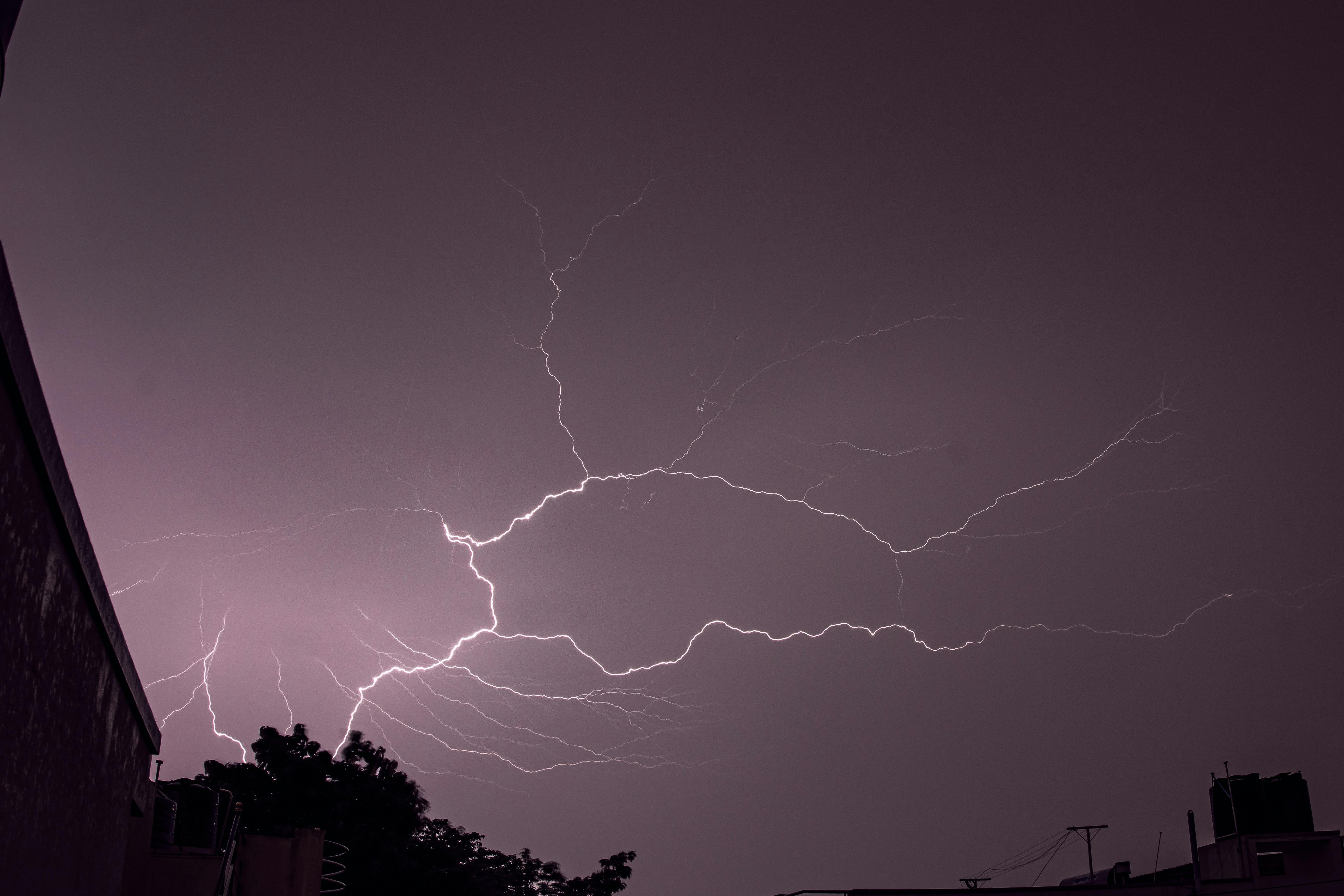 Dramatic long exposure photo of lightning striking across a night sky over buildings.