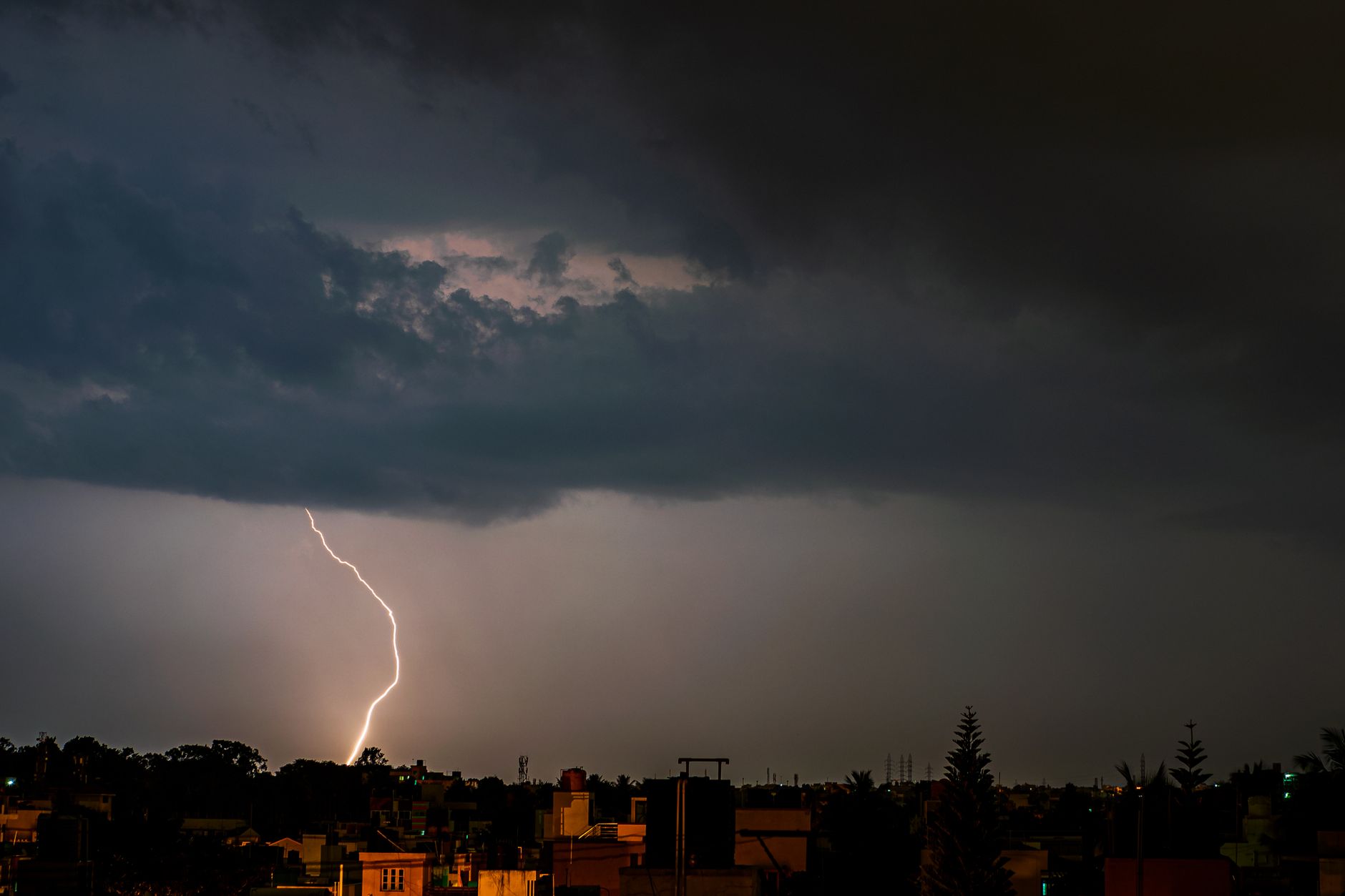 A powerful lightning strike illuminates the cityscape under dark storm clouds, showcasing nature's raw power at night.
