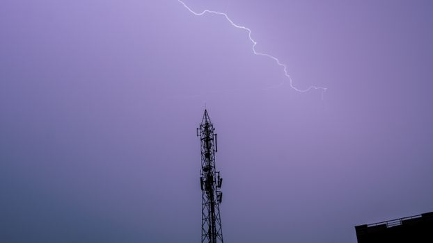 A striking image of lightning illuminating the sky above a cell tower, captured at night.