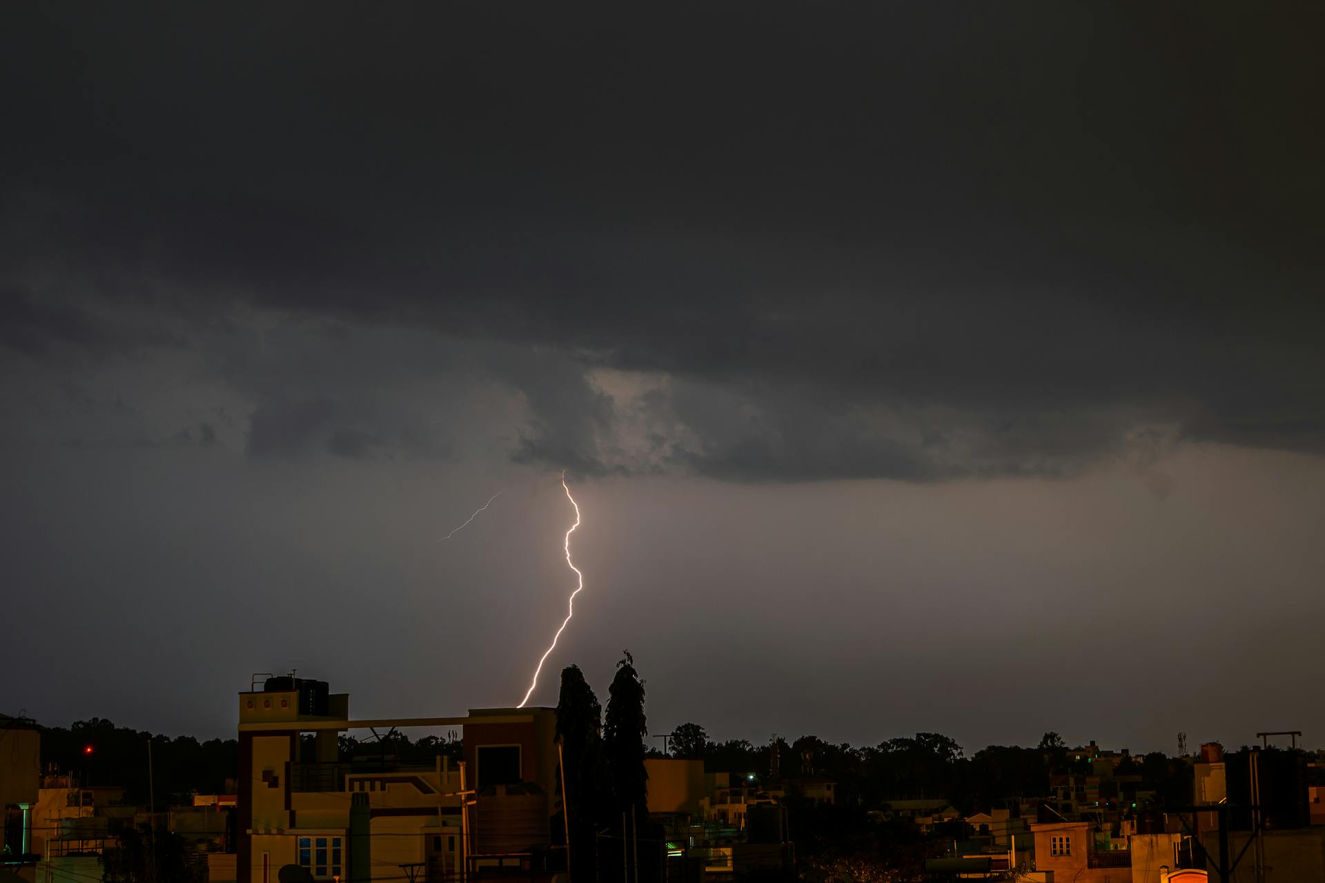 A powerful lightning strike illuminates a dark cityscape under stormy skies.