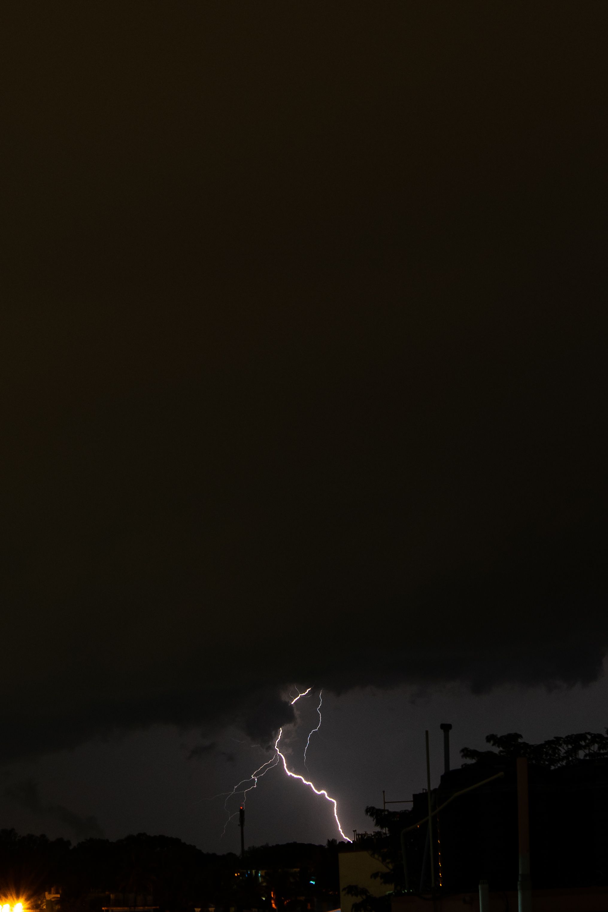 Captivating lightning bolt piercing through dark storm clouds with city lights below, showcasing nature's power.