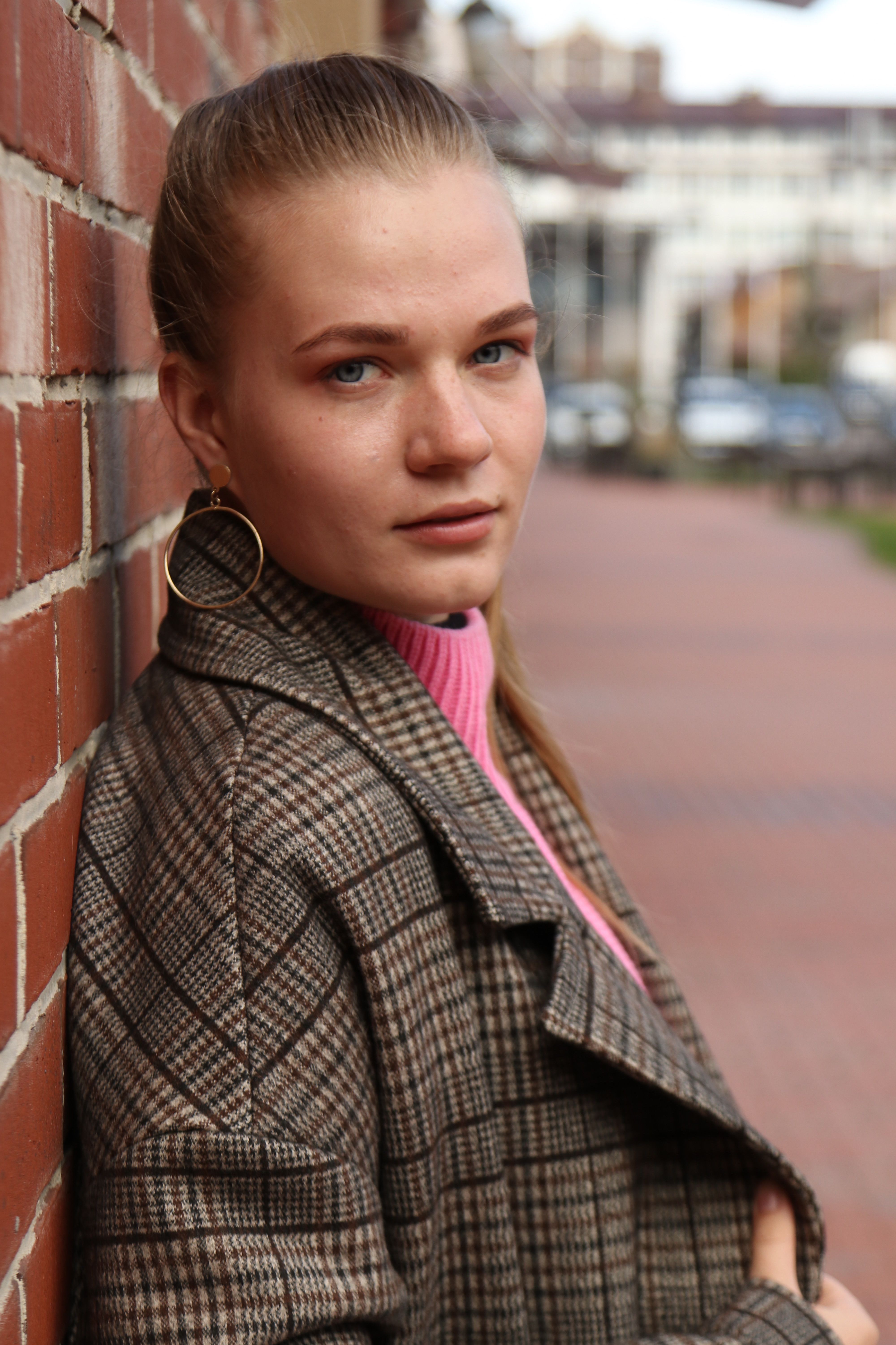 Fashionable young woman leaning against a brick wall outdoors.