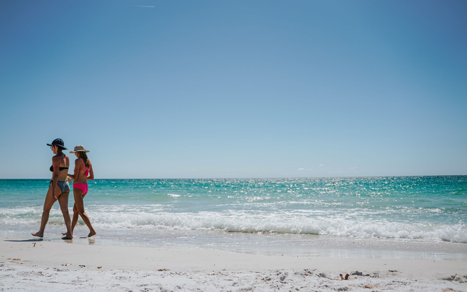 Two women walking along the sunny shoreline of Belleair Beach, FL, enjoying the ocean breeze.