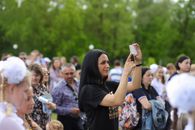 A woman in a crowd taking a photo with a smartphone during a daylight outdoor event.
