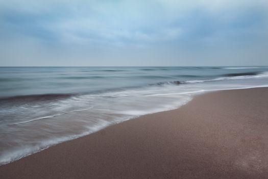Tranquil ocean waves softly crashing on a sandy shoreline under a cloudy sky.