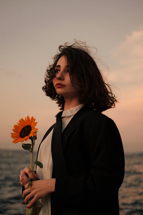 Free A Woman Holding a Sunflower by the Seaside Stock Photo