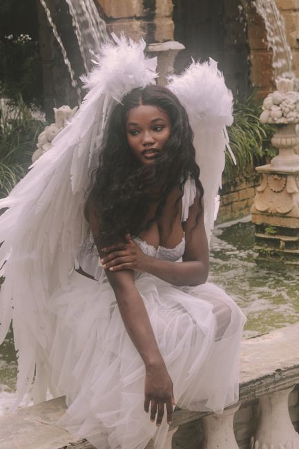 A woman in an angel costume with white wings sitting gracefully by a fountain.
