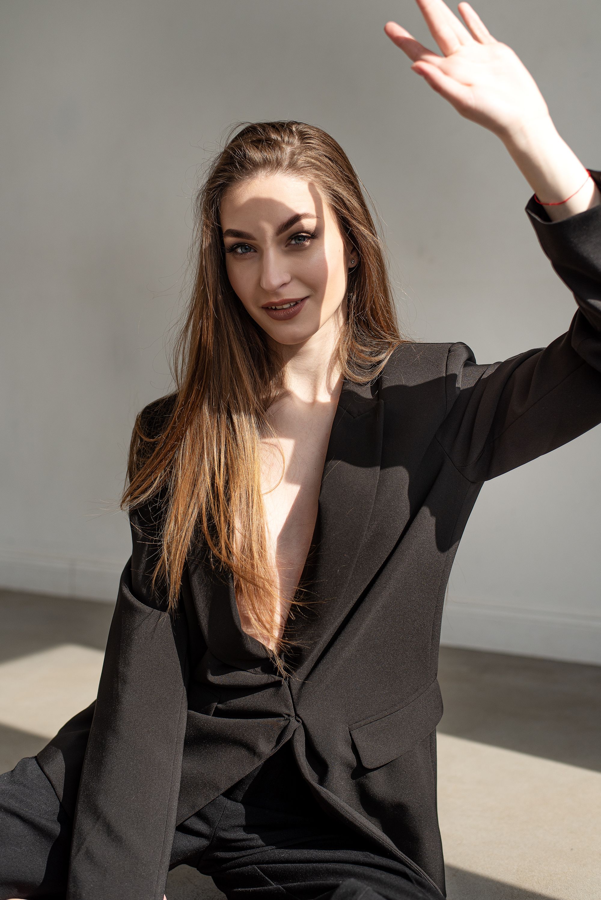 Stylish portrait of a woman in a black blazer waving in a modern indoor setting.