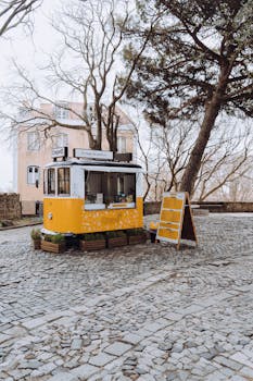 A cozy yellow food stall selling crepes on a serene cobblestone street surrounded by trees.
