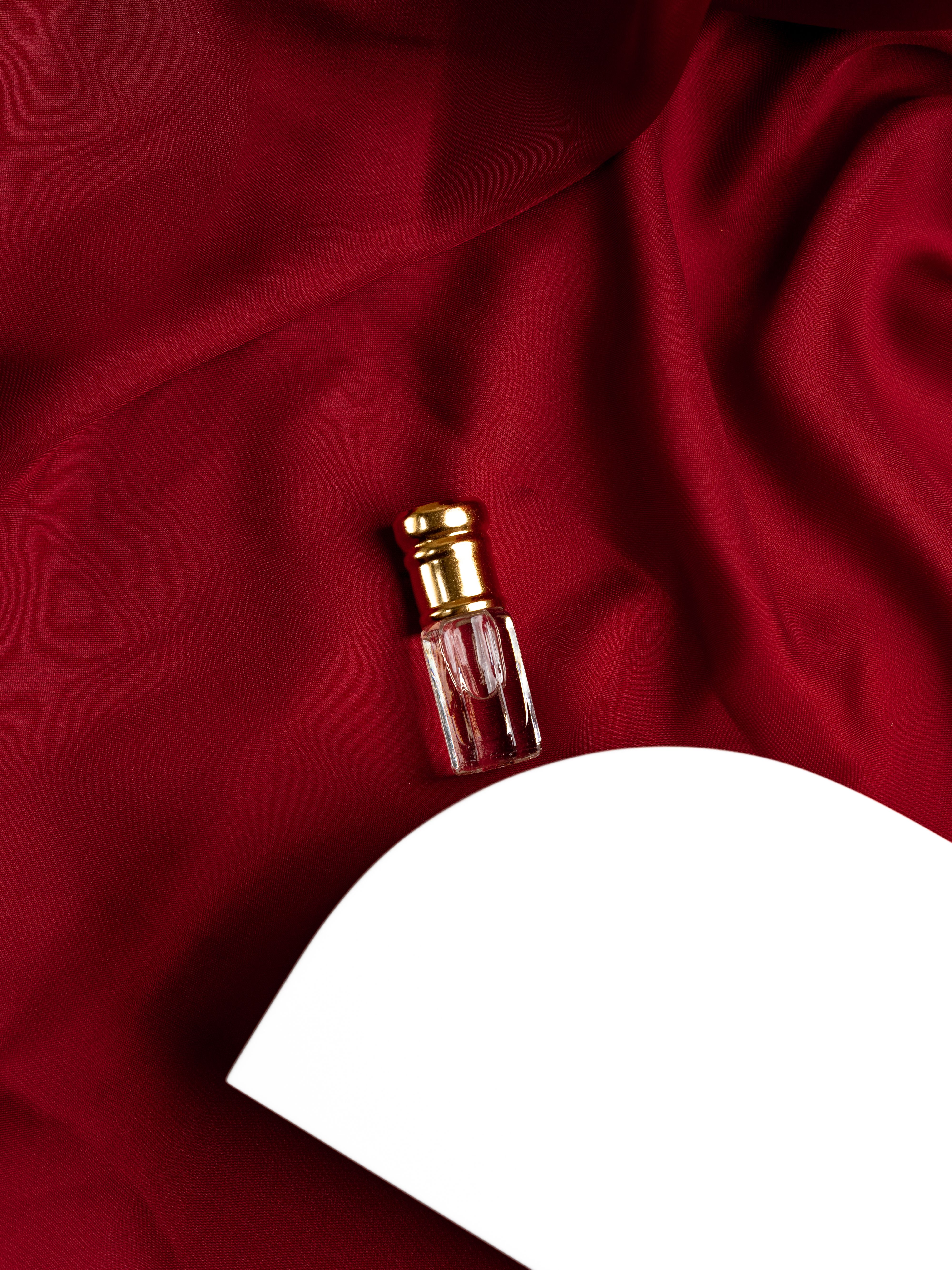 A glass perfume bottle rests elegantly on luxurious red silk fabric, accompanied by a white platform.
