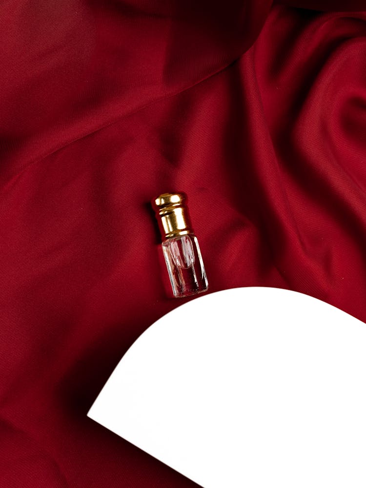 Perfume Bottle On A Red Silky Fabric Beside While Platform