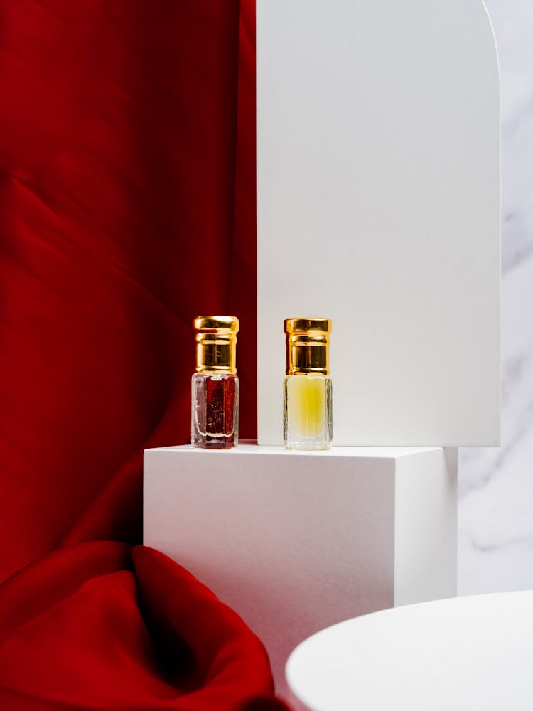 Perfume Bottles On White Platform Near Red Silky Fabric