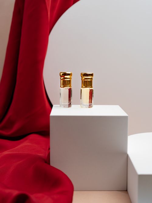 Free Two gold-capped perfume bottles on a white platform with red fabric backdrop, perfect for product showcases. Stock Photo