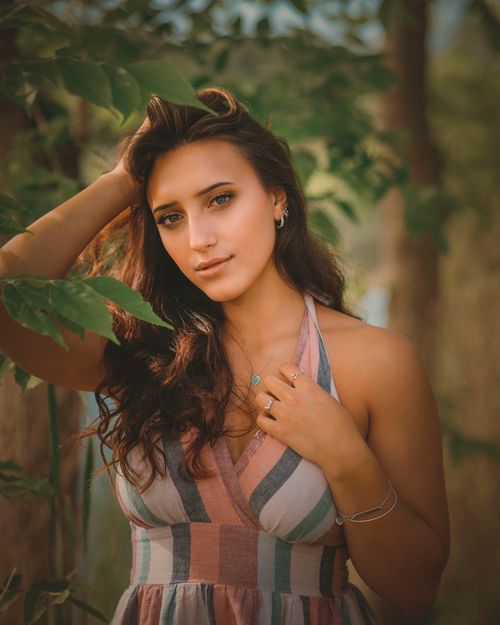Free Portrait of a woman with curly hair standing amidst green foliage in an outdoor setting. Stock Photo