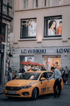 Photo by Fatih Sucu Yellow taxi in front of LC Waikiki store with people walking on a busy street.