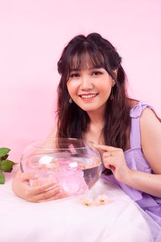 Young woman in a purple dress holding a fishbowl with flowers, smiling.
