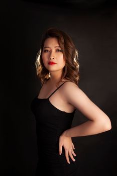 Studio portrait of a confident young woman in a black dress on a dark background.