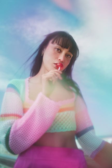 Artistic portrait of a woman with a lollipop against a dreamy sky backdrop.