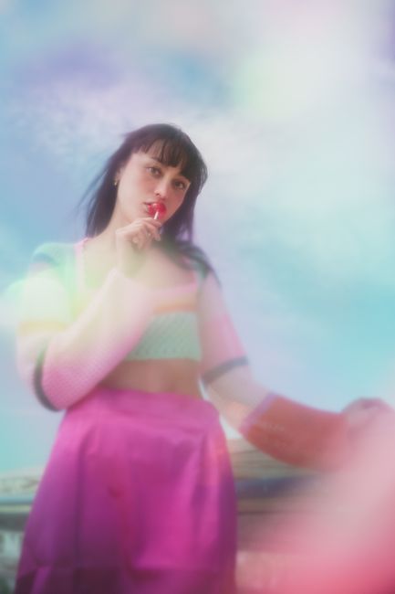 A dreamy, colorful portrait of a woman holding a lollipop against a sky background.