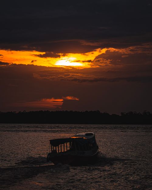 Free A lone boat sails across the water as the sun sets, creating a dramatic and colorful sky. Stock Photo